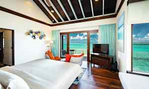 Interiör av ett rum med säng, fåtöljer, TV på en möbel och stora glasdörrar som visar en utsikt över havet. (AI-genererad text)