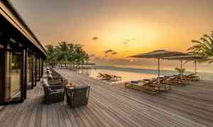 En träterrass vid en infinity-pool och havet under en kvällshimmel. (AI-genererad text)