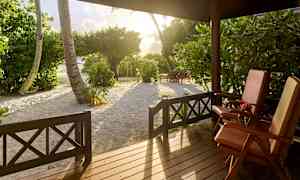 Utsikt från en veranda med två solstolar, träd och sand i solnedgångsljus. (AI-genererad text)