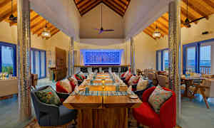 En restaurang med träbord och färgglada stolar, samt en dekorerad bakvägg och stora fönster. (AI-genererad text)