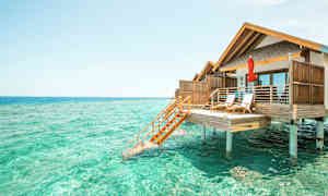 Fotografi av en bungalow på pålar över turkost vatten. (AI-genererad text)