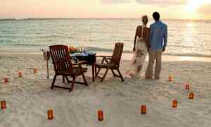Ett par står på en strand vid havet, framför en dukad bord med stolar och ljus. (AI-genererad text)