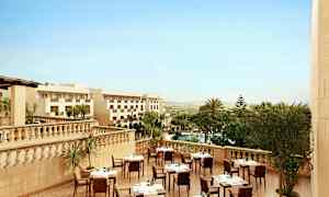 Hotellets utomhusterrass med dukade bord, omgiven av palmer och utsikt över landskapet. (AI-genererad text)