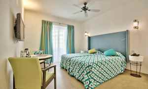 Ett hotellrum med en dubbelsäng, dekorativa kuddar, och ett bord med två stolar. (AI-genererad text)