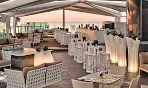 En lounge med moderna möbler, bord, soffor och en bardisk under ett täckt tak. (AI-genererad text)