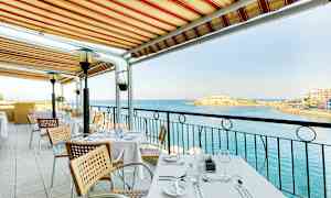 Ett bord på en utomhusterrass under en markis med utsikt över havet. (AI-genererad text)