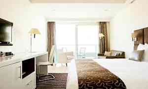 Ett hotellrum med en stor säng, skrivbord, stol, soffa och balkong med glasdörrar. (AI-genererad text)