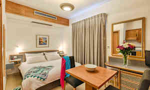 Ett ljust hotellrum med en dubbelsäng, matbord, sittplatser och en spegel. Dekorerat med en blomvas på bordet. (AI-genererad text)