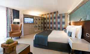 Ett hotellrum med en dubbelsäng, en fåtölj, ett bord och en tv på väggen. (AI-genererad text)