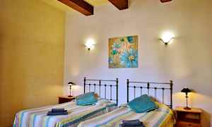 Ett sovrum med två enkelsängar, vägglampor och en blå blomstermålning på väggen. (AI-genererad text)