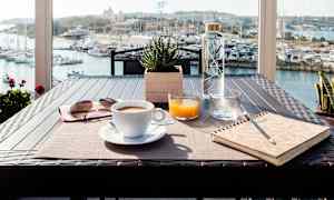 Frukostbord placerat på en terrass med utsikt över en marina. (AI-genererad text)