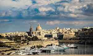 Vy över en stad med kupolförsedd byggnad och båtar i en hamn. (AI-genererad text)