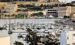 En marina med många båtar, omgiven av historiska byggnader och frodig vegetation. (AI-genererad text)