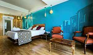 Ett hotellrum med en stor säng, dekorativ väggmålning, träinredning och två röda fåtöljer framför ett bord. (AI-genererad text)