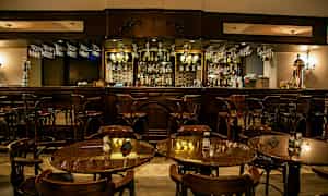 En elegant bar med träinredning och bordsgrupper med stolar i förgrunden. (AI-genererad text)