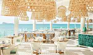 En ljus restaurang med rottinglampor och utsikt över havet. (AI-genererad text)