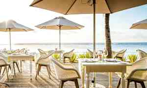 En utomhusrestaurang med bord och parasoller vid havet. (AI-genererad text)