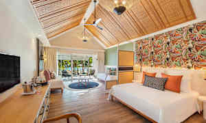 Ett elegant hotellrum med säng, sittgrupp och utsikt över trädgård genom skjutdörrar. (AI-genererad text)