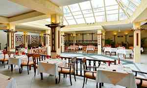 En rymlig restaurang med stora fönster och bord med vitdukade bordsuppsättningar. (AI-genererad text)