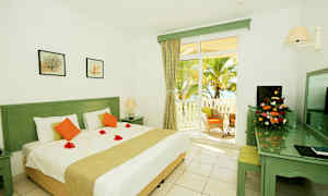 Vitrum med en stor säng, dekorativa blomblad på täcket och uteplatsdörr mot en palmträdgård. (AI-genererad text)