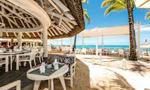 En öppen restaurang vid stranden med vita möbler och utsikt över havet. (AI-genererad text)