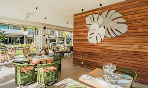 En utomhusrestaurang med grönskande möbler och en väggdekoration av stora blad. (AI-genererad text)