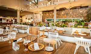 Interiör av en restaurang med träbord och stolar, väggar av sten, upphängda lampor och grönska som dekoration. (AI-genererad text)