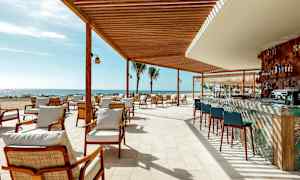 En utomhusrestaurang med sittplatser och en bar under en träpaviljong vid stranden. (AI-genererad text)