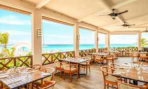 Restaurang med terrass som har bord och stolar, utsikt över havet och stranden. (AI-genererad text)