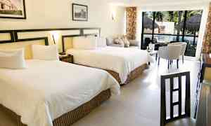 Bild av ett hotellrum med två stora sängar, sittgrupp och ett bord framför stora fönster som vetter mot en pool. (AI-genererad text)