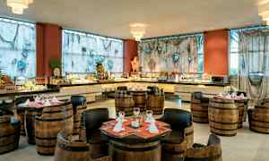 Ett restaurangområde med kärlstolar och bord, omgiven av ett buffébord och dekorerade gardiner. (AI-genererad text)