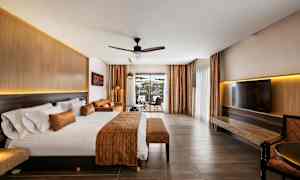 Hotellrum med stor säng, sittgrupp och utsikt genom glasdörrar. (AI-genererad text)