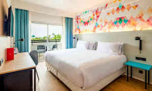 Ett hotellrum med en dubbelsäng, färgglad väggritning, skrivbord, och balkong med två stolar. (AI-genererad text)