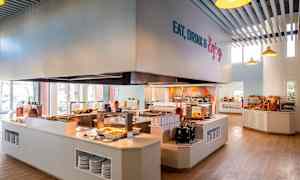 En cafeteria med självservering, där mat presenteras på diskar och brödutbud syns på hyllor. (AI-genererad text)