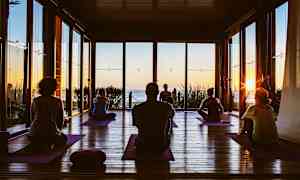 Personer som utövar yoga på mattor i en sal med utsikt över havet vid solnedgången. (AI-genererad text)