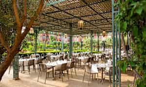 En utomhusservering med bord och stolar under ett trärastertak. (AI-genererad text)