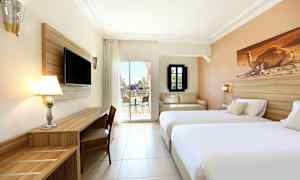 Bild av ett hotellrum med två sängar, TV, skrivbord och en sittgrupp, samt utsikt mot en terrass. (AI-genererad text)