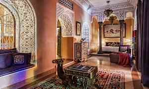 Ett elegant inrett rum med dekorativa gipsmönster, arkitektoniska bågar, orientaliska möbler och varm belysning. Ett bord formad som en kamel står på en färgglad matta. (AI-genererad text)