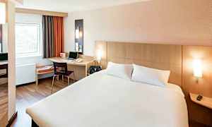 Hotellrum med en dubbelsäng, ett skrivbord med en stol och ett fönster. (AI-genererad text)