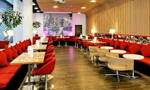 Atmosfärisk restaurang med röda sittplatser, små bord och en fondvägg av en svartvit stadsbild. (AI-genererad text)