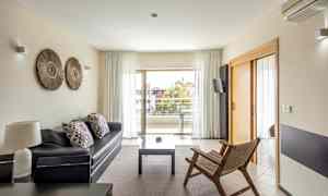 Ett modernt vardagsrum med soffa, trästol och acces till balkong genom glasdörrar. (AI-genererad text)