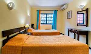 Ett hotellrum med två enkelsängar, en väggspegel, skrivbord och fönster med färgglada gardiner. (AI-genererad text)