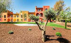 Byggnader målade i gult och rött med arkader, omgivna av träd och anlagda grönområden. (AI-genererad text)