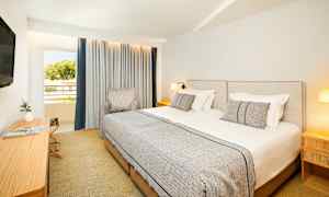 Hotellrum med två enkelsängar, en stol, en skrivbord och en TV, samt ett fönster med gardiner. (AI-genererad text)