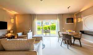 Ett vardagsrum med moderna möbler och en matplats, med stora fönster som visar en trädgård utanför. (AI-genererad text)