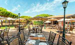 Uteservering med bord och stolar, samt parasoller under en klar blå himmel. (AI-genererad text)