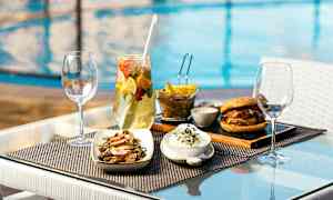 Mat på ett bord vid poolen, bestående av sallad, hamburgare, pommes frites och dryck. (AI-genererad text)