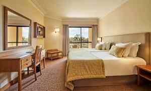 Bild av ett hotellrum med en dubbelsäng, arbetsbord och stolar samt en balkong med utsikt. (AI-genererad text)