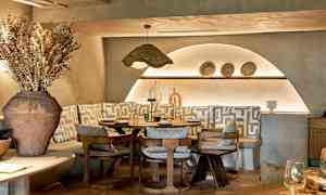 Ett stilfullt restaurangbord omgiven av stolar och bänkar med geometriska mönstrade kuddar. (AI-genererad text)