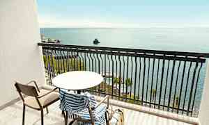 En balkong med ett bord, stol och randig handduk, med havsutsikt. (AI-genererad text)
